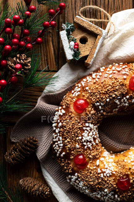 Top view of appetizing cut homemade round bread with hole decorated with sprinkles and cherry placed on wooden table with Christmas decoration — Stock Photo