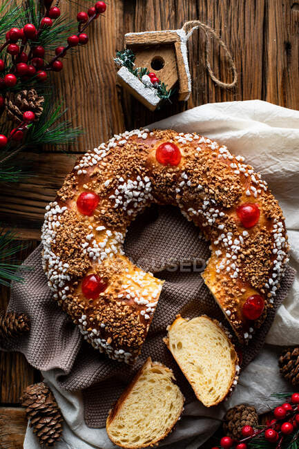 Vista superior do apetitoso pão redondo caseiro cortado com furo decorado com polvilhas e cereja colocada em mesa de madeira com decoração de Natal — Fotografia de Stock