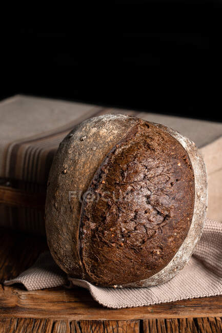 Здоровий свіжий домашній житній хліб, розміщений на дерев'яному столі з тканиною на чорному тлі — стокове фото