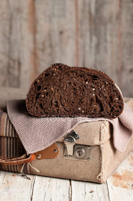 Pão de centeio escuro saudável apetitoso com grãos cortados ao meio colocados na mala de tecido retro na mesa de madeira rasgada — Fotografia de Stock