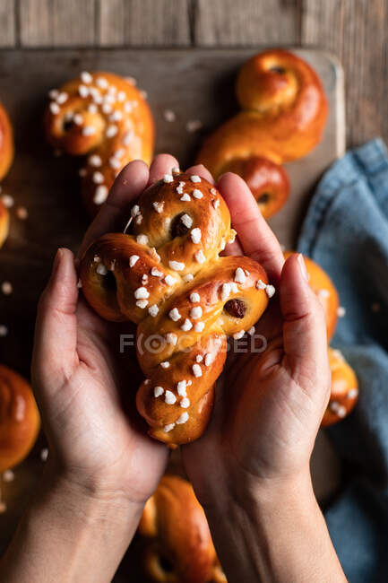 Crop anonymous person in cozy gray sweater and jeans holding traditional fresh baked saffron buns with raisin and sprinkles — Stock Photo