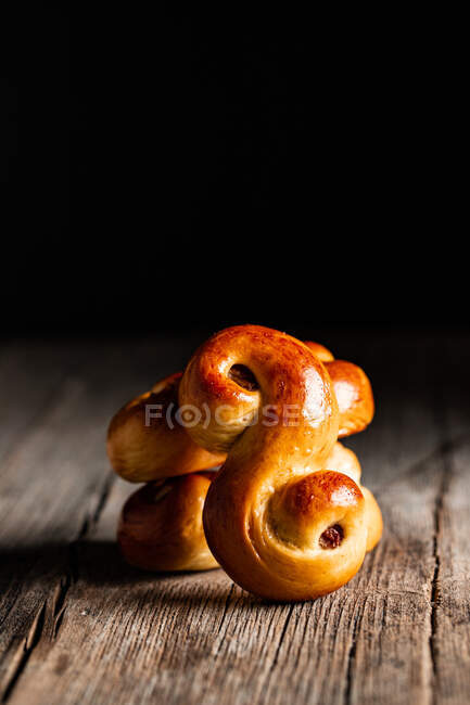 Delicious fresh baked traditional saffron buns with raisin placed on wooden table against black background — Stock Photo