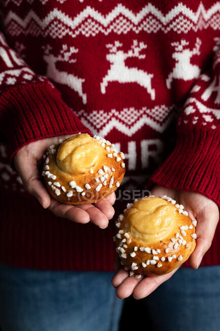 Colture femminili in maglione rosso di Natale e jeans con pasticceria fatta in casa e dimostrando gustosi panini freschi con spruzzi bianchi — Foto stock