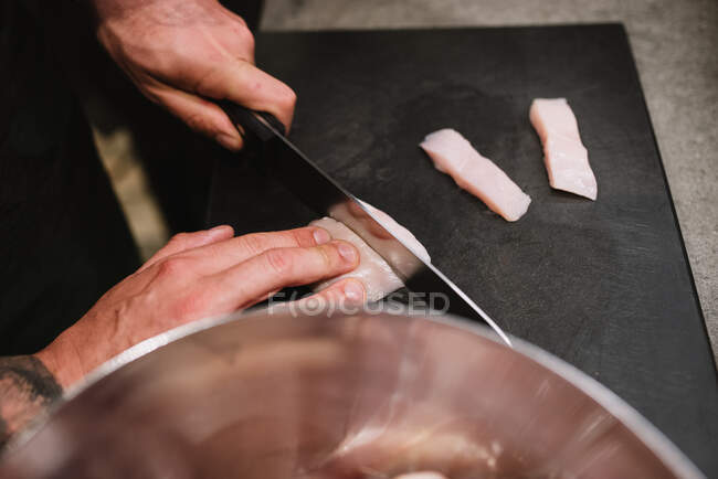 Da suddetta persona anonima affettare petto di pollo fresco vicino a ciotola di metallo durante il corso di cucina del ristorante in Navarra, Spagna — Foto stock
