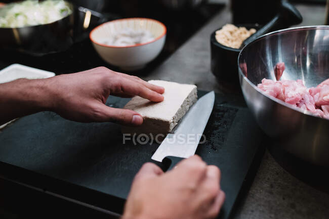 De cima do chef anônimo cortando pedaço de queijo fresco perto da tigela com carne durante a aula de culinária na cozinha do restaurante em Navarra, Espanha — Fotografia de Stock