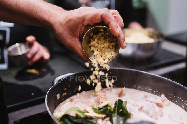 Crop chef spilling fresh ingredient into pan with stew while preparing dinner during cooking lesson in restaurant in Navarre, Spain — Stock Photo