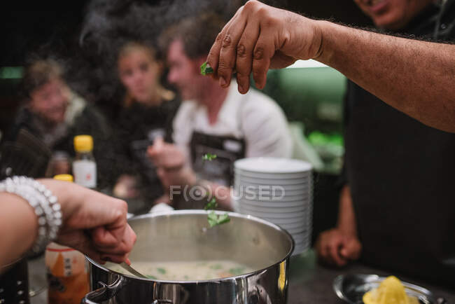 Personas irreconocibles agregando ingredientes en una cacerola con un delicioso plato durante la clase de cocina en un restaurante en Navarra, España - foto de stock