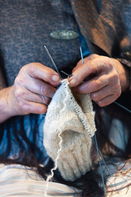 Неузнаваемая пожилая женщина, использующая иглы для вязания теплой одежды из натуральной пряжи — стоковое фото