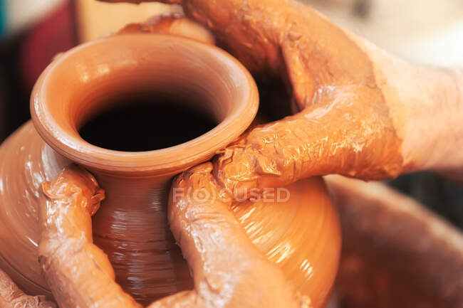Крупный план анонимный ремесленник, делающий вазу из глины во время работы в профессиональной керамике — стоковое фото