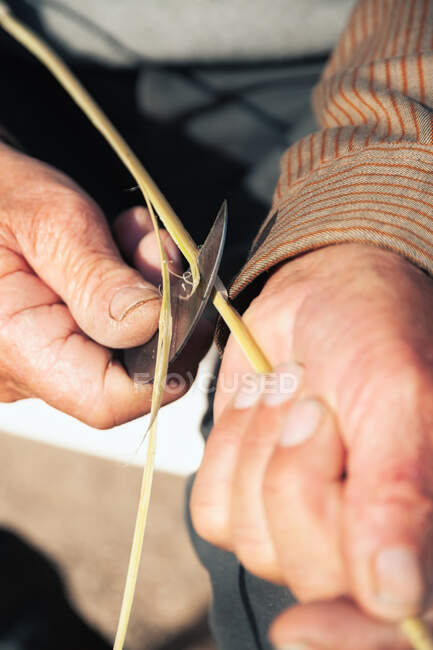 Зверху анонімний невідомий ремісник, який використовує ніж для різання рослинної палички під час виготовлення плетеного матеріалу — стокове фото
