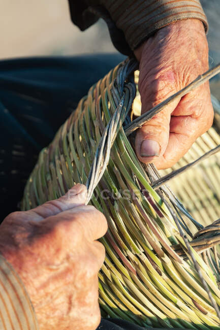 Unrecognizable elderly craftsman making authentic wicker basket on sunny day — Stock Photo