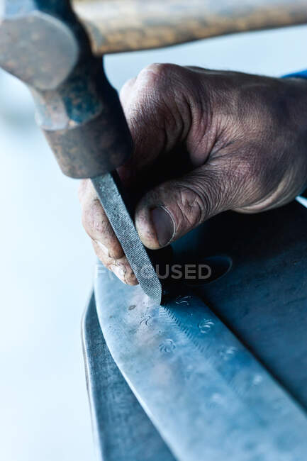 Невідомий літній майстер, який вдарив стамеску молотком при створенні прикраси на сталевому ножі — стокове фото