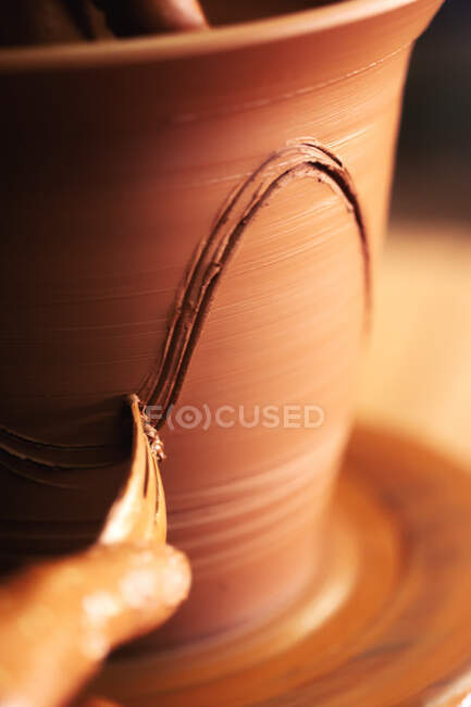 Неузнаваемый ремесленник, использующий вилку, чтобы царапать волну на глиняном горшке во время работы в мастерской — стоковое фото