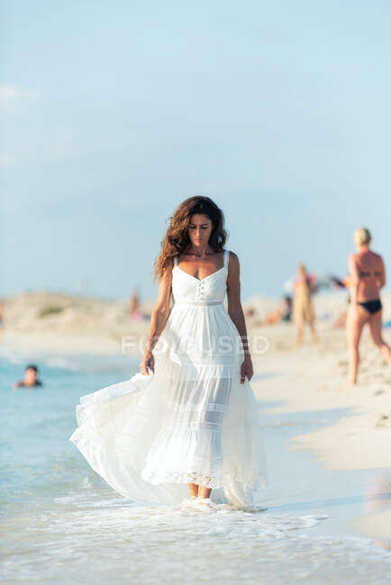 Frau in hellweißem Kleid geht am Strand spazieren und schaut nach unten — Stockfoto