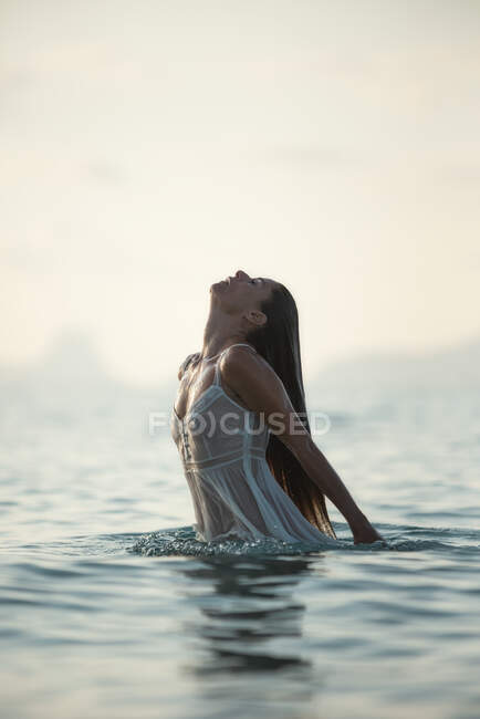 Сексуальна жінка в напівпрозорому мокрому платті виходить з морської води тихим вечором — стокове фото