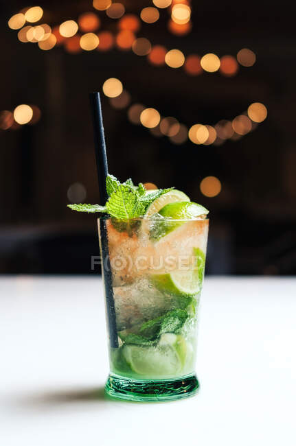 Glass cup of cold mojito with straw placed on counter against blurred background in pub — Stock Photo