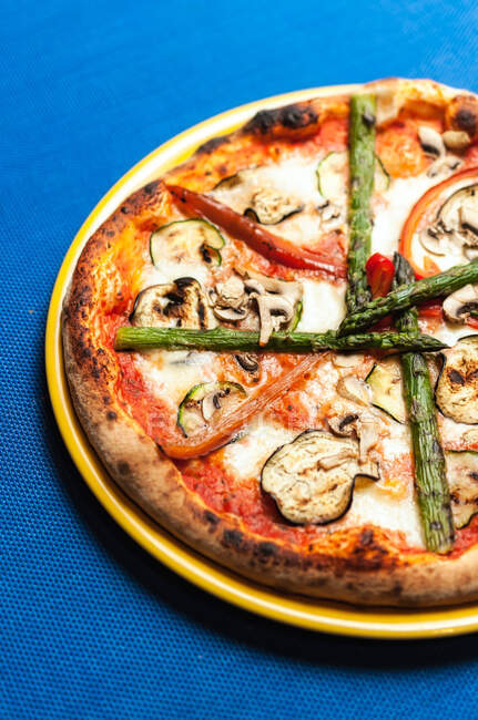 De arriba la pizza sabrosa con hortalizas puestas en el plato al mantel azul en la cafetería - foto de stock