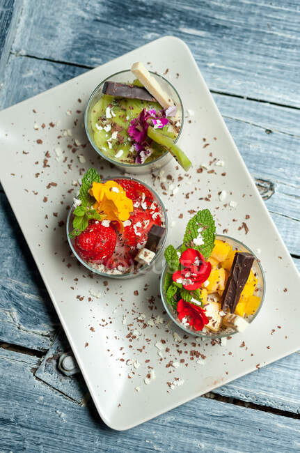 Vue du dessus des tasses avec divers desserts tropicaux placés sur un plateau sur une table en bois au restaurant — Photo de stock