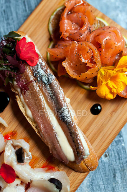 Top view of delicious fish sandwiches decorated with flowers placed on wooden board in restaurant — Stock Photo
