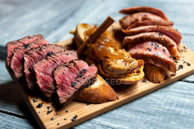 Torradas frescas com pedaços de carne assada e crua colocados em tábua de madeira na mesa do restaurante — Fotografia de Stock