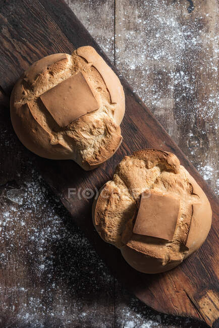 Vista superior de pães de pão fresco colocados em tábua de madeira velha na mesa coberta com farinha na padaria — Fotografia de Stock