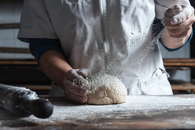 Unrecognizable person kneading dough with flour on table while working in bakery — Stock Photo