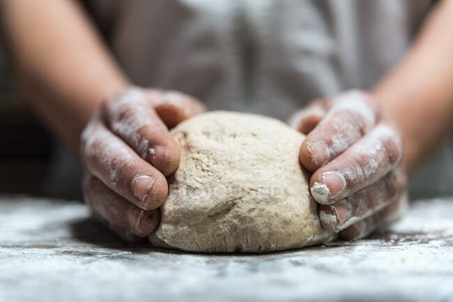 Неузнаваемый человек смешивает тесто с мукой на столе во время работы в пекарне — стоковое фото