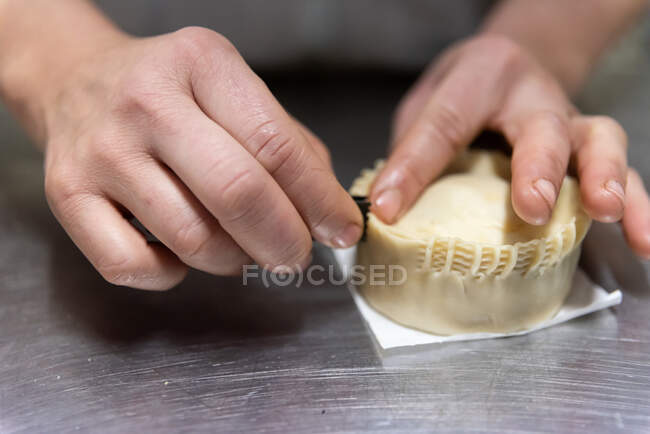Крупним планом анонімний чоловік нарізає пиріг скоринкою на металевий стіл в сучасній пекарні — стокове фото