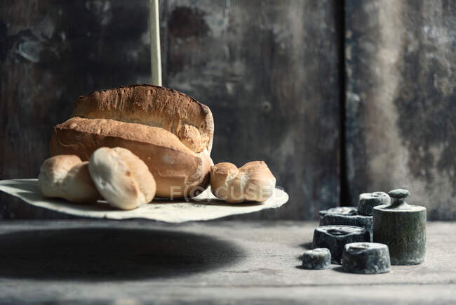 Laib frisches Brot und weiche Brötchen auf Retro-Waagen in der Nähe schmutzige Gewichte gegen schäbige Wand in Bäckerei platziert — Stockfoto