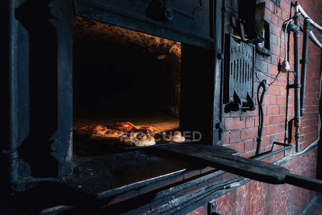 Набір свіжих булочок, поміщених всередину гарячої цегляної печі в професійній пекарні — стокове фото