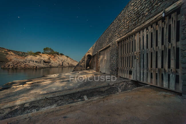 Edifício de pedra envelhecida com portões de madeira localizados contra o céu estrelado noturno na praia de Cala Es Canaret, Ibiza, Espanha — Fotografia de Stock