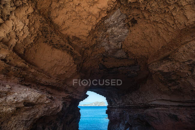 Rugosa passagem arqueada de caverna de pedra que leva ao mar azul pacífico em Cala Conta no dia ensolarado em Ibiza, Espanha — Fotografia de Stock