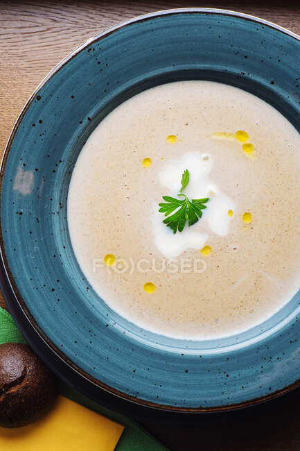 Верхний вид вкусного сливочного супа с грибами порчини, украшенными листьями петрушки, подаваемых в голубой тарелке — стоковое фото