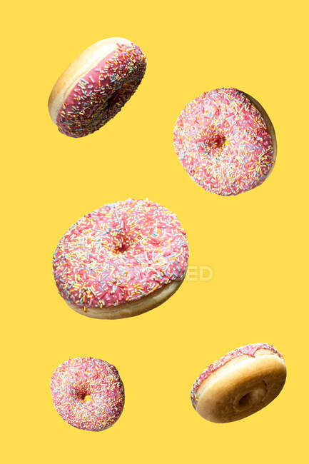Рожеві солодкі пончики, що плавають на жовтому тлі — стокове фото
