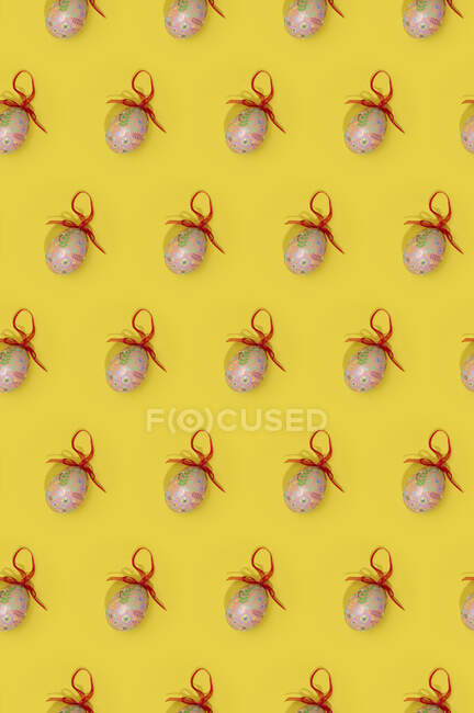 Padrão de Páscoa sem costura com ovos coloridos decorados com fitas vermelhas dispostas em linhas no fundo amarelo — Fotografia de Stock