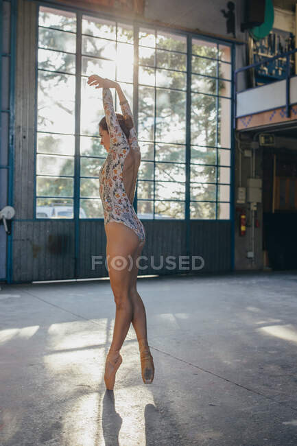 Vue latérale de la jeune ballerine gracieuse en costume de corps coloré et pointes dansant sur la pointe des pieds tout en s'entraînant dans un studio de lumière — Photo de stock