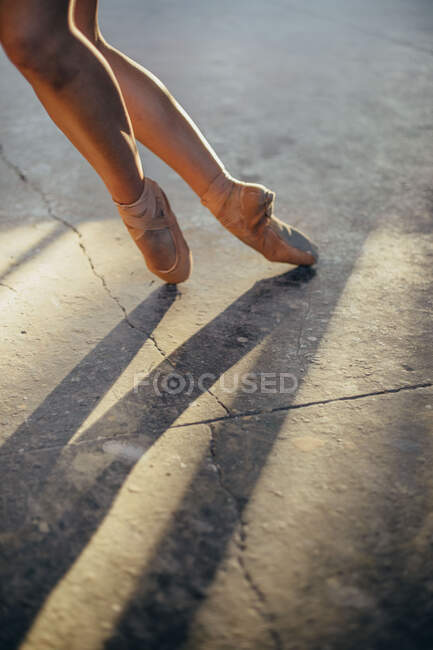 Cropped image of female ballet dancer in pointes with bruise on leg standing on tiptoe while performing classic exercise during training in studio — Stock Photo