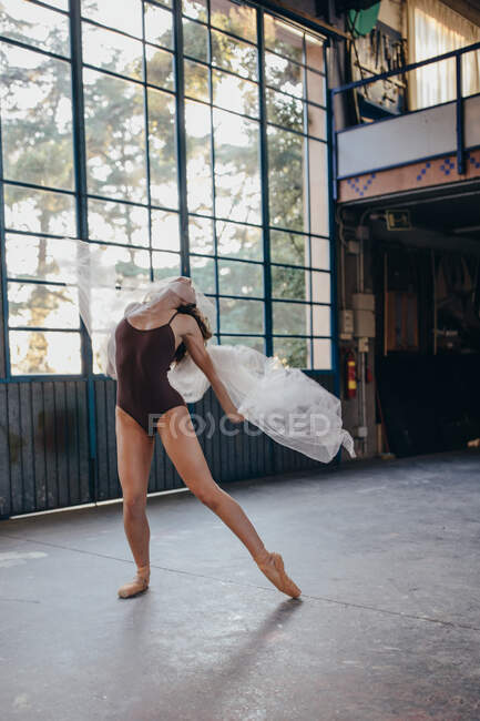 Молода драматична жіноча танцівниця в чорному боді-костюмі виконує чуттєвий танець з тюлем під час тренувань наодинці в легкій просторій студії — стокове фото