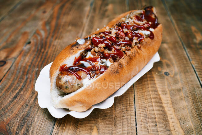 From above of tasty appetizing hot dog with sausage and sauces served on white plate on wooden table — Stock Photo
