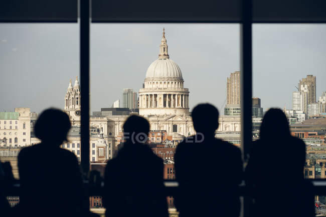 Back view silhouettes of travelers standing near window at viewpoint and admiring view of Saint Paul Cathedral in London — Stock Photo