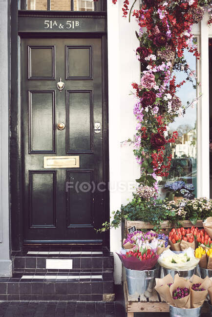Puesto de madera con ramos de flores situado en la calle de la ciudad cerca de la puerta negra del edificio residencial en la ciudad - foto de stock