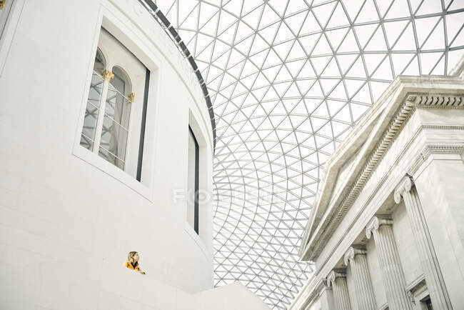 Von unten steht die Frau auf der Terrasse außerhalb des weißen Ziergebäudes und bewundert die geometrische Kuppeldecke im modernen Pavillon — Stockfoto