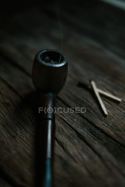 Du dessus de la vieille pipe à fumer et des allumettes placées sur une table à bois rugueuse dans une pièce sombre — Photo de stock