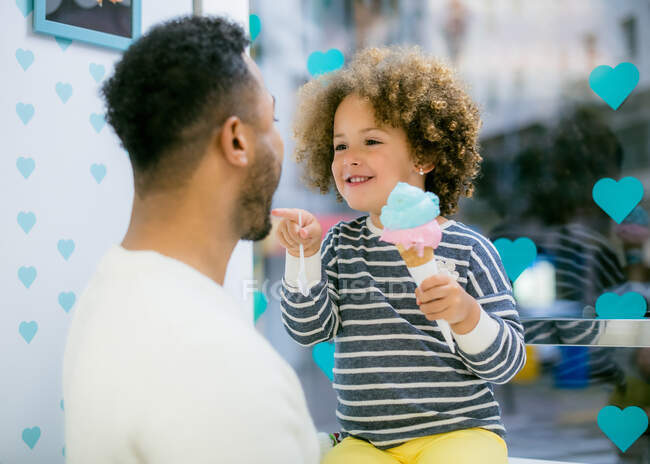 Encantadora menina étnica encaracolado segurando cone doce de sorvete brincando com o pai amoroso preto no café — Fotografia de Stock