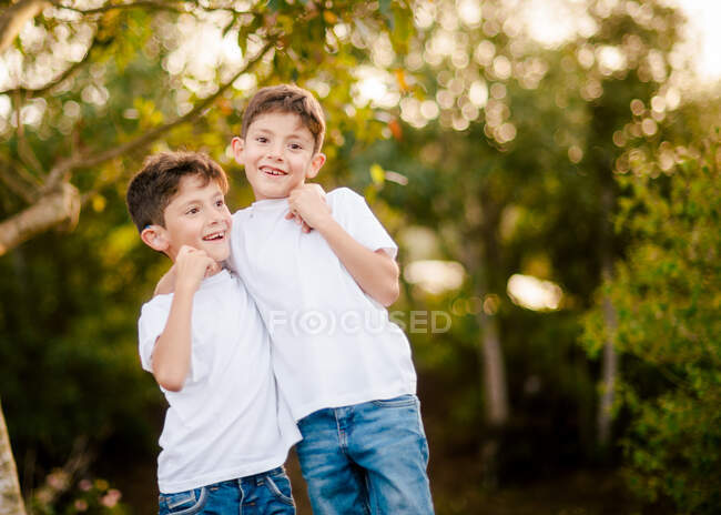 Meninos gêmeos felizes abraçando e olhando para a câmera no parque — Fotografia de Stock