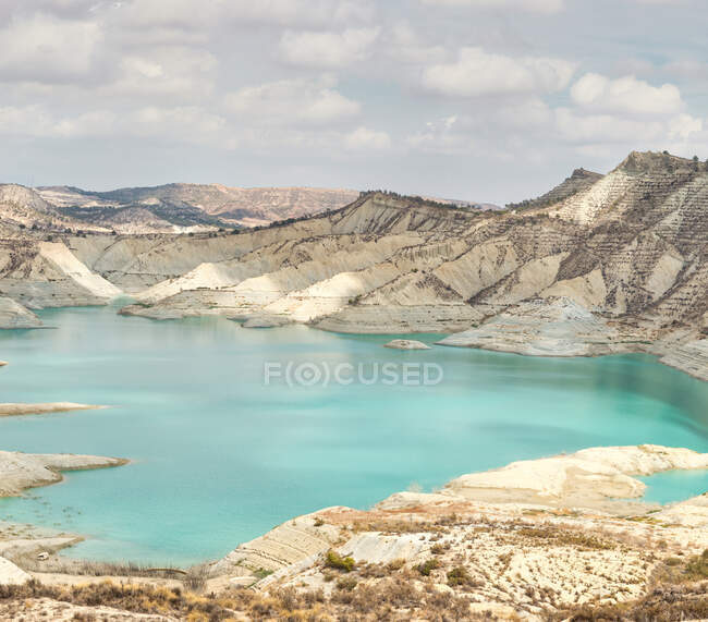 Reservatório de água limpa localizado entre a costa com grama seca e montanha áspera em dia nublado em Algeciras, Espanha — Fotografia de Stock