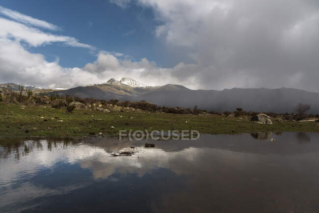 Pintoresca vista del cielo nublado sobre la montaña y el tranquilo agua del lago en la naturaleza - foto de stock