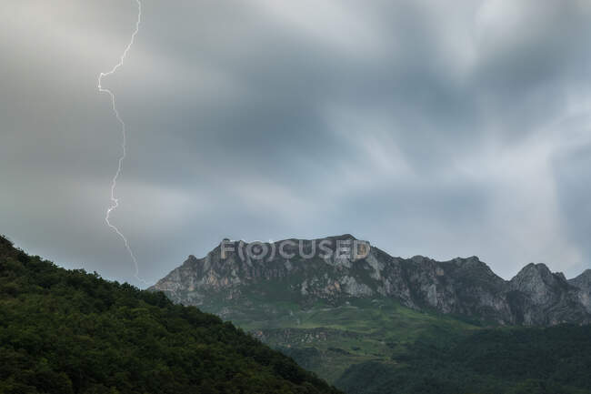 Majestic long exposure view of thin lightning striking mountain range against overcast sky on stormy day in nature — Stock Photo