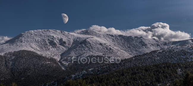 Breathtaking wide angle view of snowy mountain range against evening sky with white clouds and moon in nature — Stock Photo