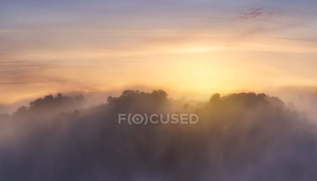Cordilheira montanhosa com árvores localizadas contra o céu brilhante do nascer do sol na manhã nebulosa na natureza — Fotografia de Stock